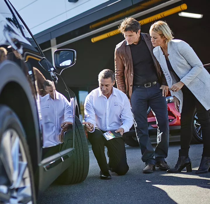 Vendeur qui inspecte la roue d'un véhicule Mazda
